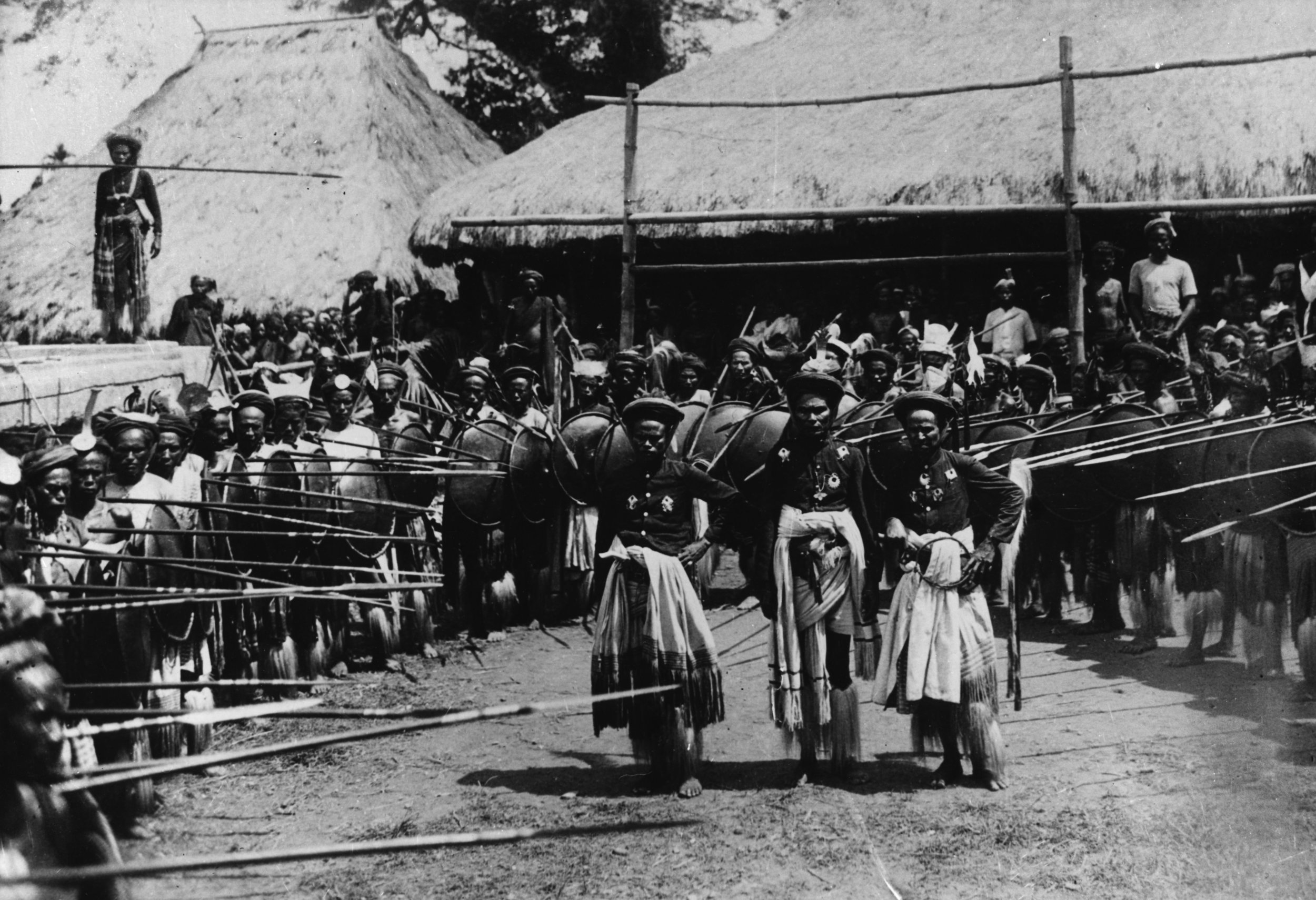 Ceremonial gathering, men in fringed hip-wraps with spears