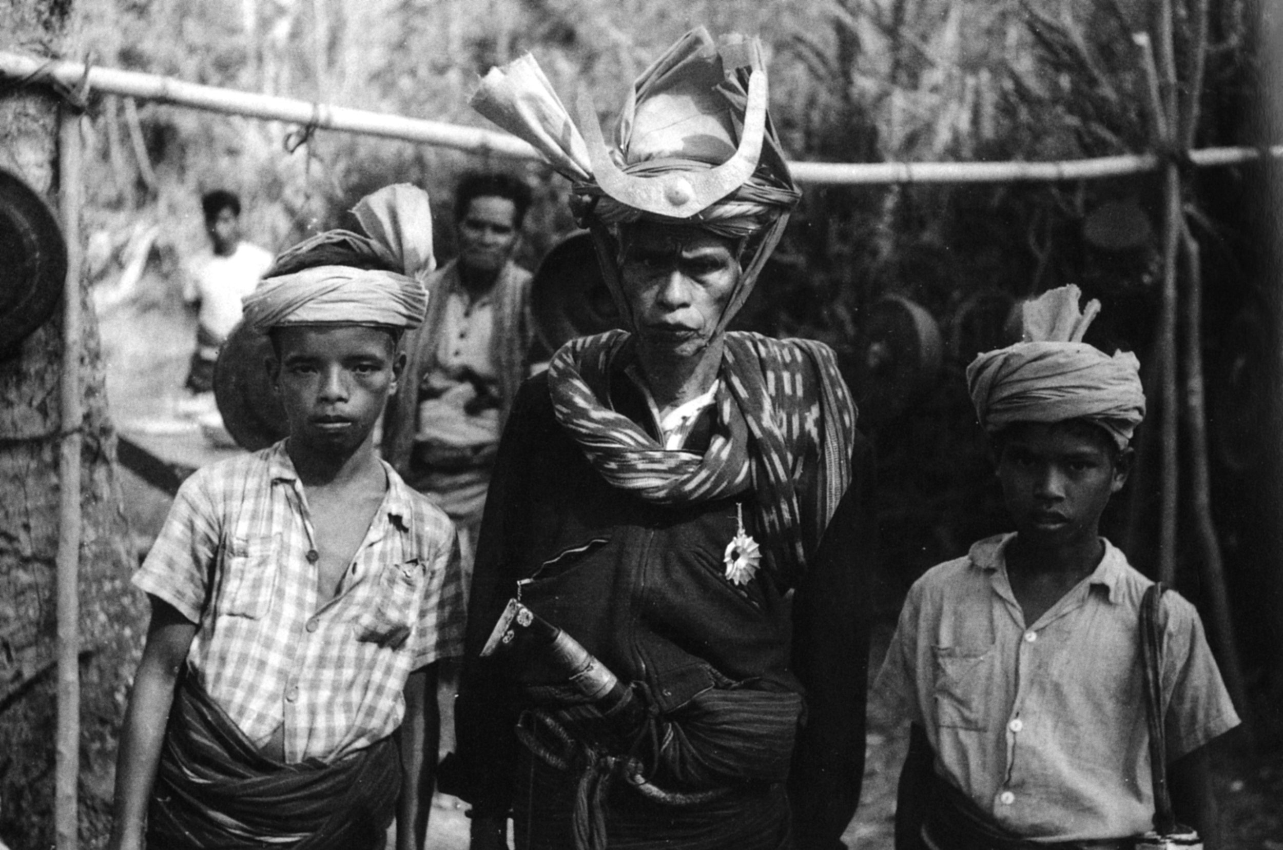 A man in an ikat shoulder cloth and head-dress with two boys